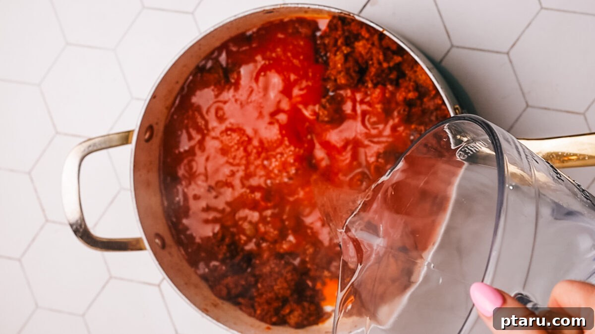 Sauce Simmered Pasta Perfection 9 Water being poured into the meat and tomato mixture in the pot.