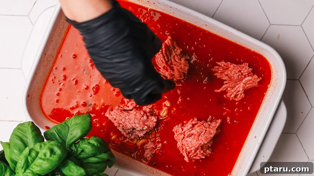 Classic Comfort Hamburger Bake 6 Raw ground beef crumbled and spread over the pasta and sauce mixture in the baking dish.