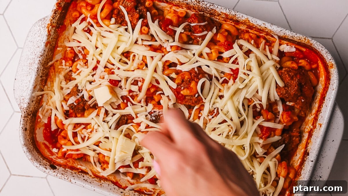 Classic Comfort Hamburger Bake 8 Shredded mozzarella cheese being spread over the partially baked casserole, preparing for final baking.