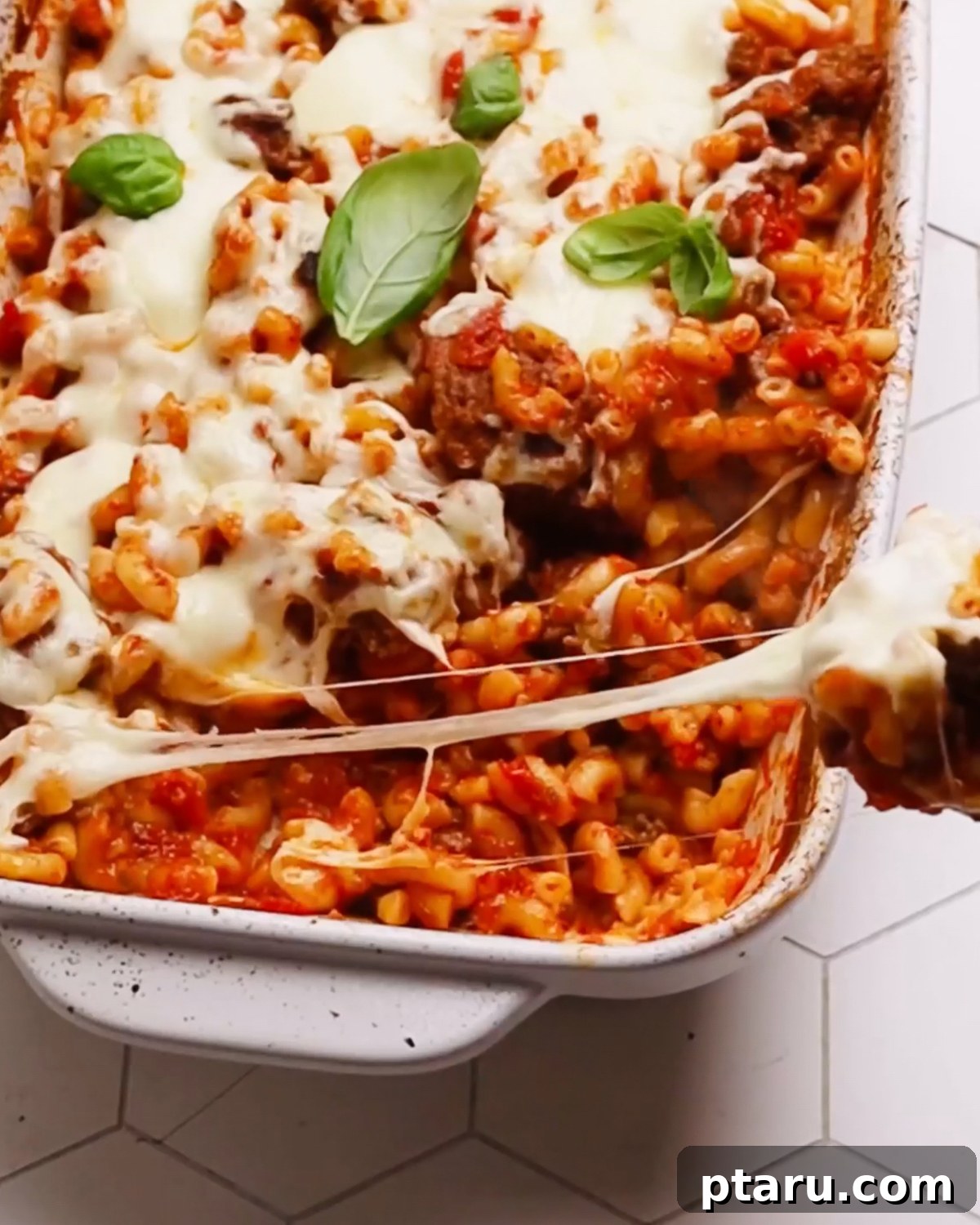 Classic Comfort Hamburger Bake 10 Close-up photo of a finished Hamburger Casserole, showing the texture of the pasta, ground beef, and melted, bubbly mozzarella cheese, garnished with fresh herbs.