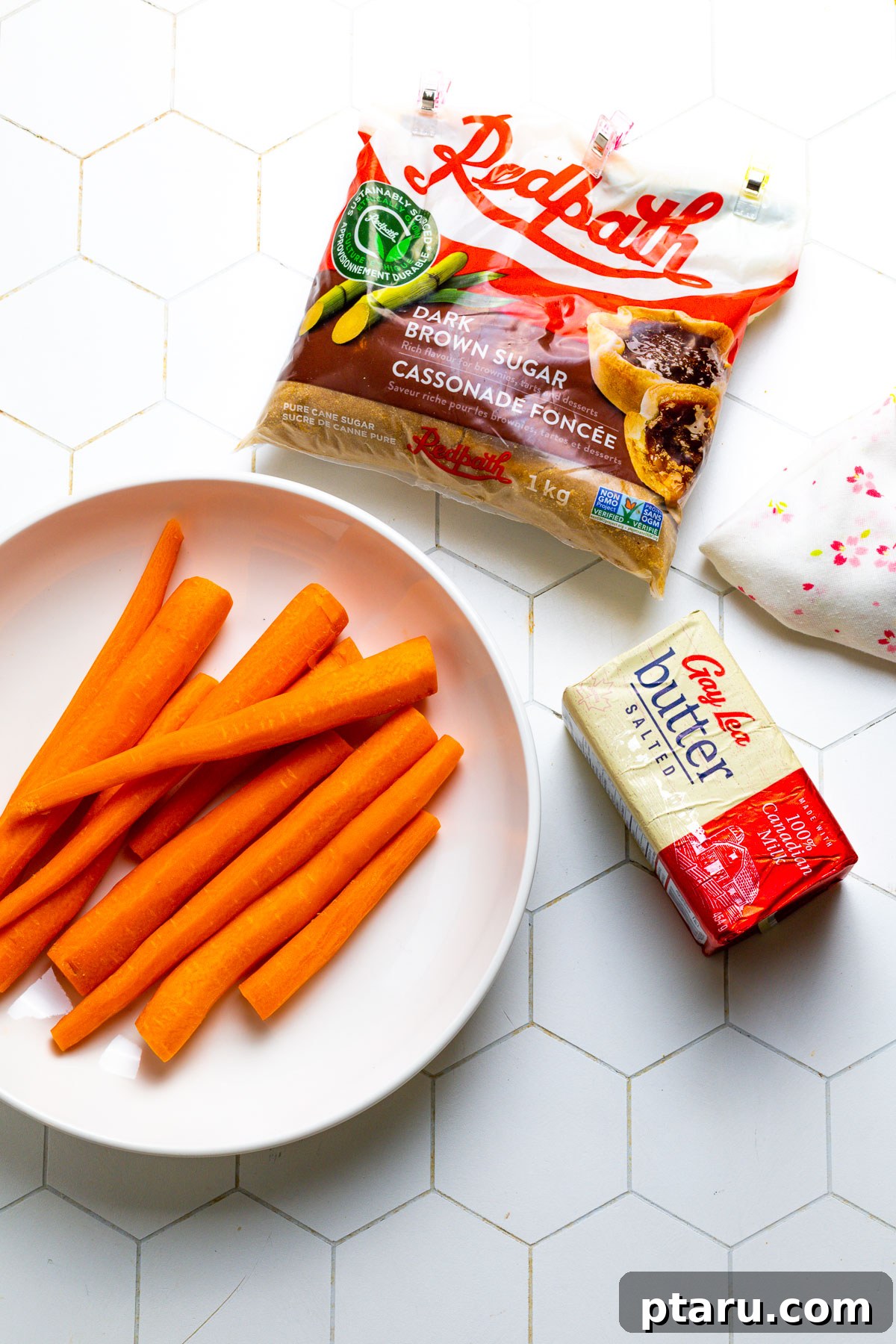 Glistening Sweet Carrots 3 Fresh carrots, salted butter, and dark brown sugar laid out, representing the main ingredients for glazed carrots.