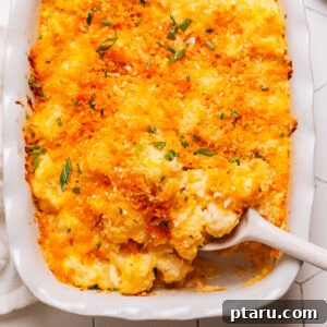 Cauliflower casserole in a baking dish with a spoon, showing its creamy interior and crispy topping.