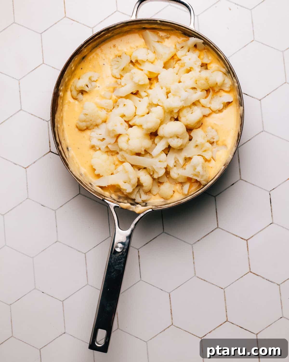 Game-Changing Cauliflower Casserole 7 Close-up of a baking dish filled with cauliflower florets coated in a creamy cheese sauce, ready for the topping.