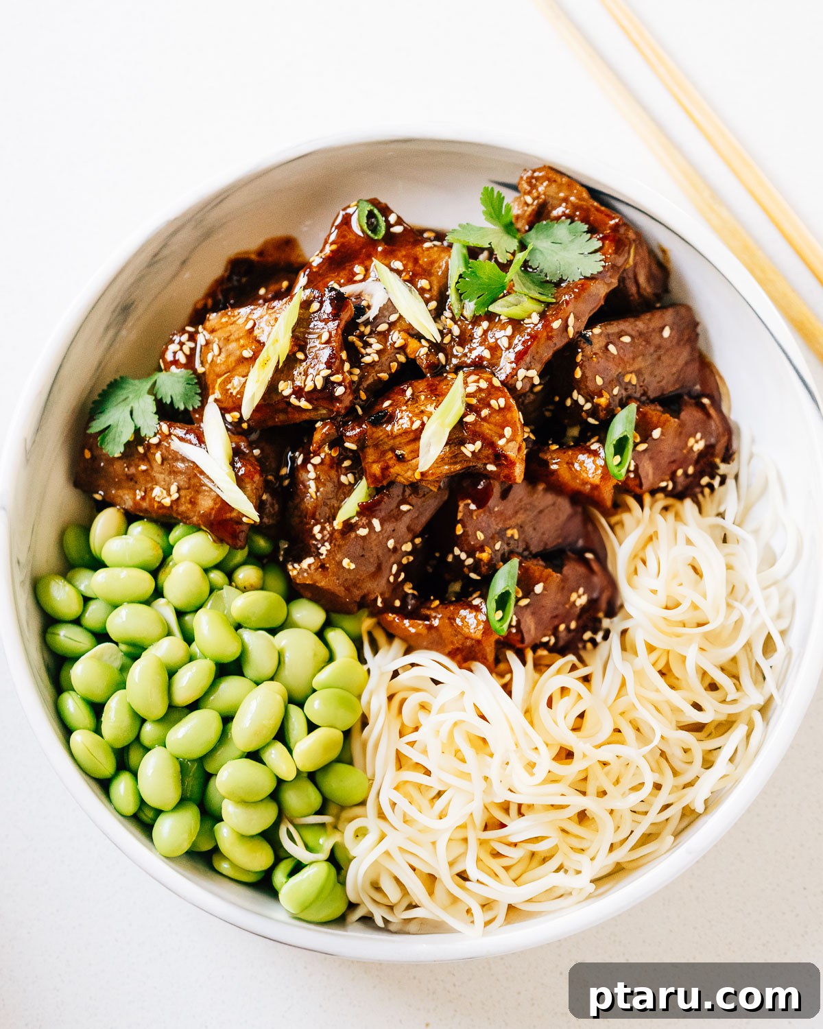 Sweet and Savory Teriyaki Beef 2 Beef teriyaki in a bowl with noodles and edamame, garnished with sesame seeds and green onions.