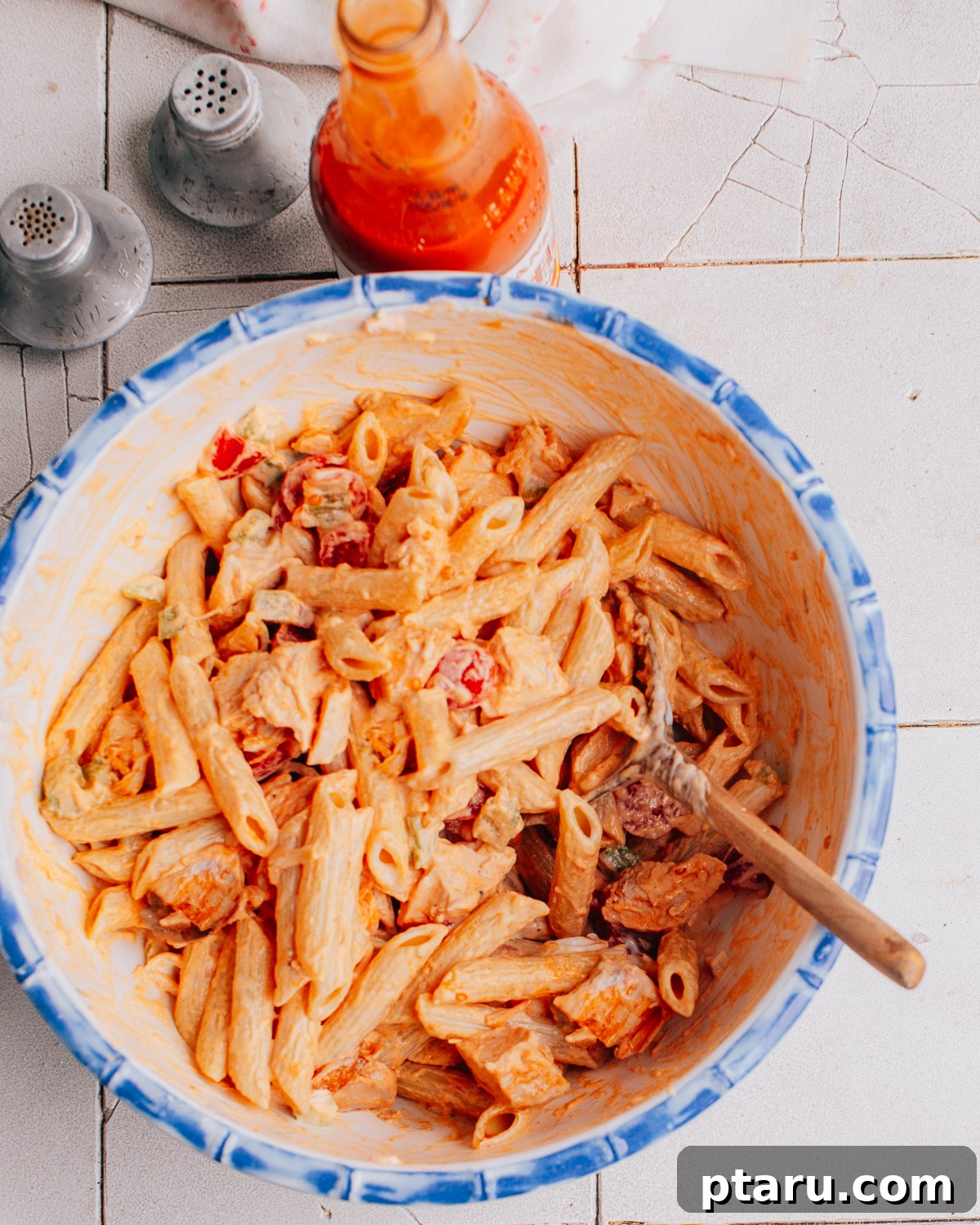 Zingy Buffalo Chicken Pasta Medley 2 A vibrant bowl of Buffalo Chicken Pasta Salad, featuring penne pasta, shredded chicken coated in buffalo sauce, diced celery, cherry tomatoes, and crumbled blue cheese, ready to be served.