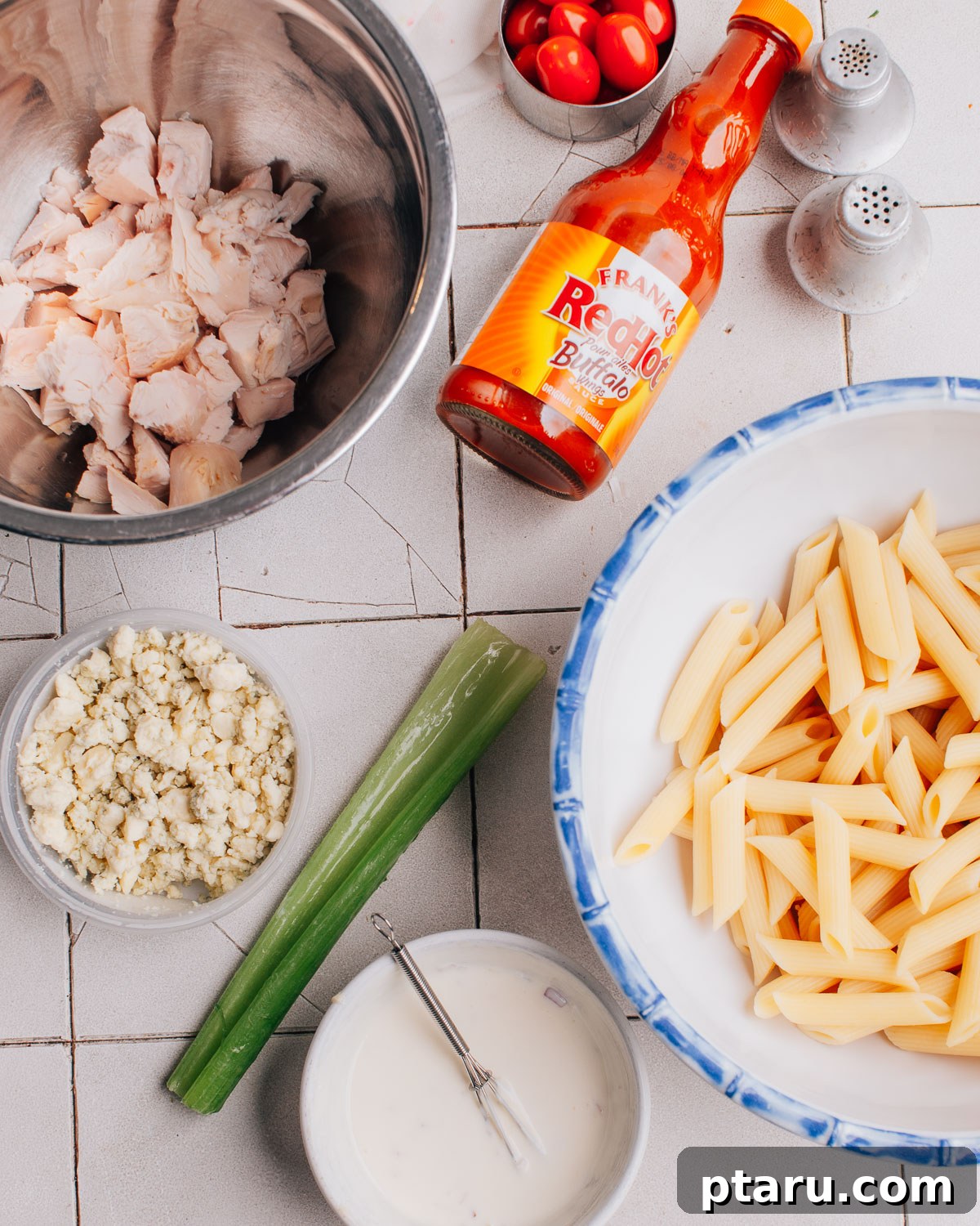 Zingy Buffalo Chicken Pasta Medley 3 All the fresh ingredients laid out for making Buffalo Chicken Pasta Salad, including pasta, cooked chicken, buffalo sauce, cherry tomatoes, celery, parsley, and blue cheese, along with dressing components.