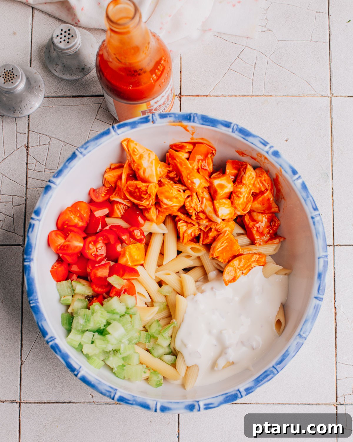 Zingy Buffalo Chicken Pasta Medley 6 Tossing shredded cooked chicken with buffalo sauce in a large mixing bowl.