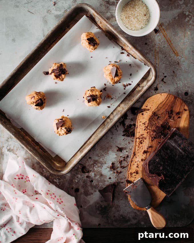 A baking tray filled with perfectly scooped coconut oatmeal cookie dough balls, some adorned with extra chocolate chips or shredded coconut, ready for the oven.