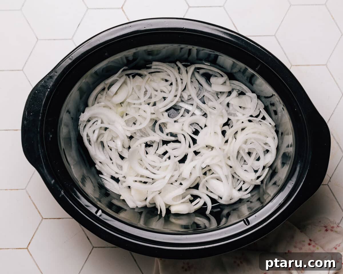 Effortless Slow Cooker BBQ Chicken 4 Sliced onions forming the base layer in the crockpot for BBQ chicken.