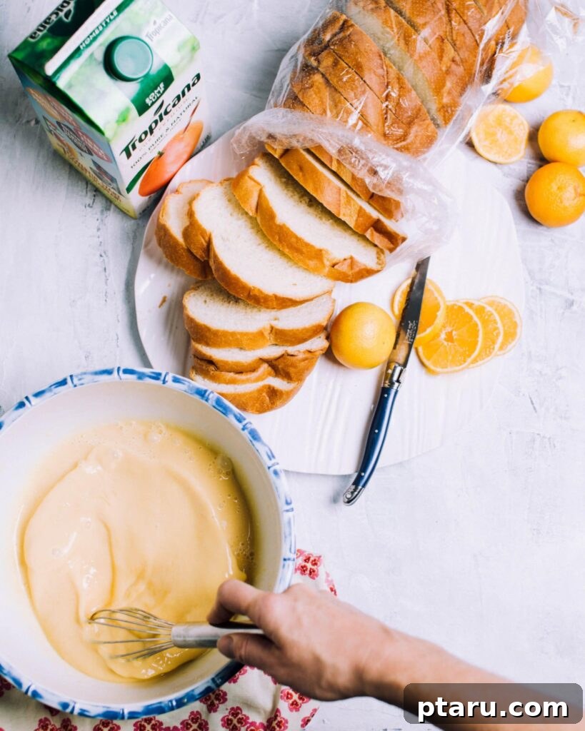Provençal Orange Bake 4 A close-up shot of a whisk blending a creamy custard with vibrant orange zest in a clear glass bowl, preparing it for an overnight French toast casserole.