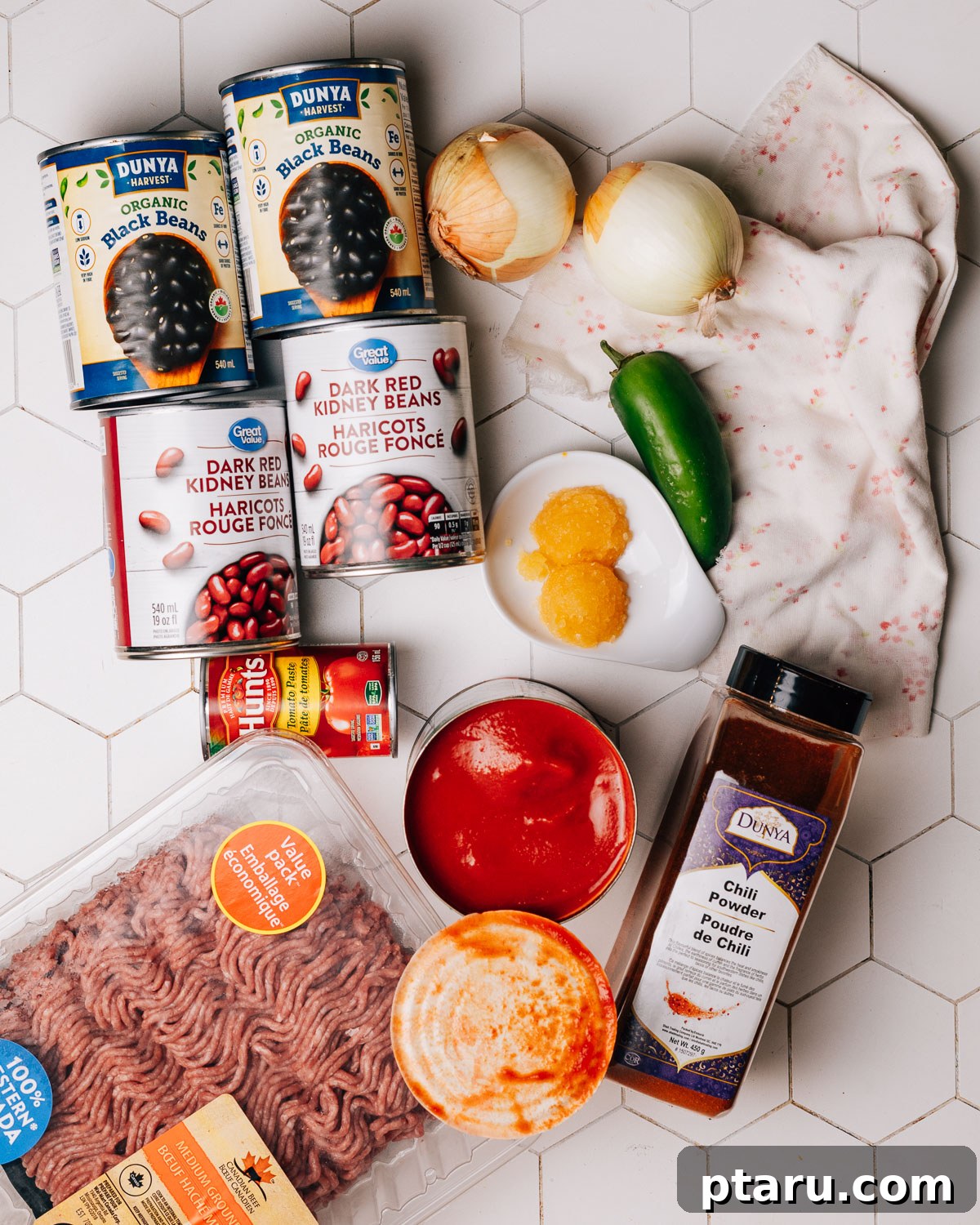 Ultimate Chili Con Carne 3 Fresh ingredients laid out for chili con carne: chili powder, ground beef, tomato paste, and jalapeños.