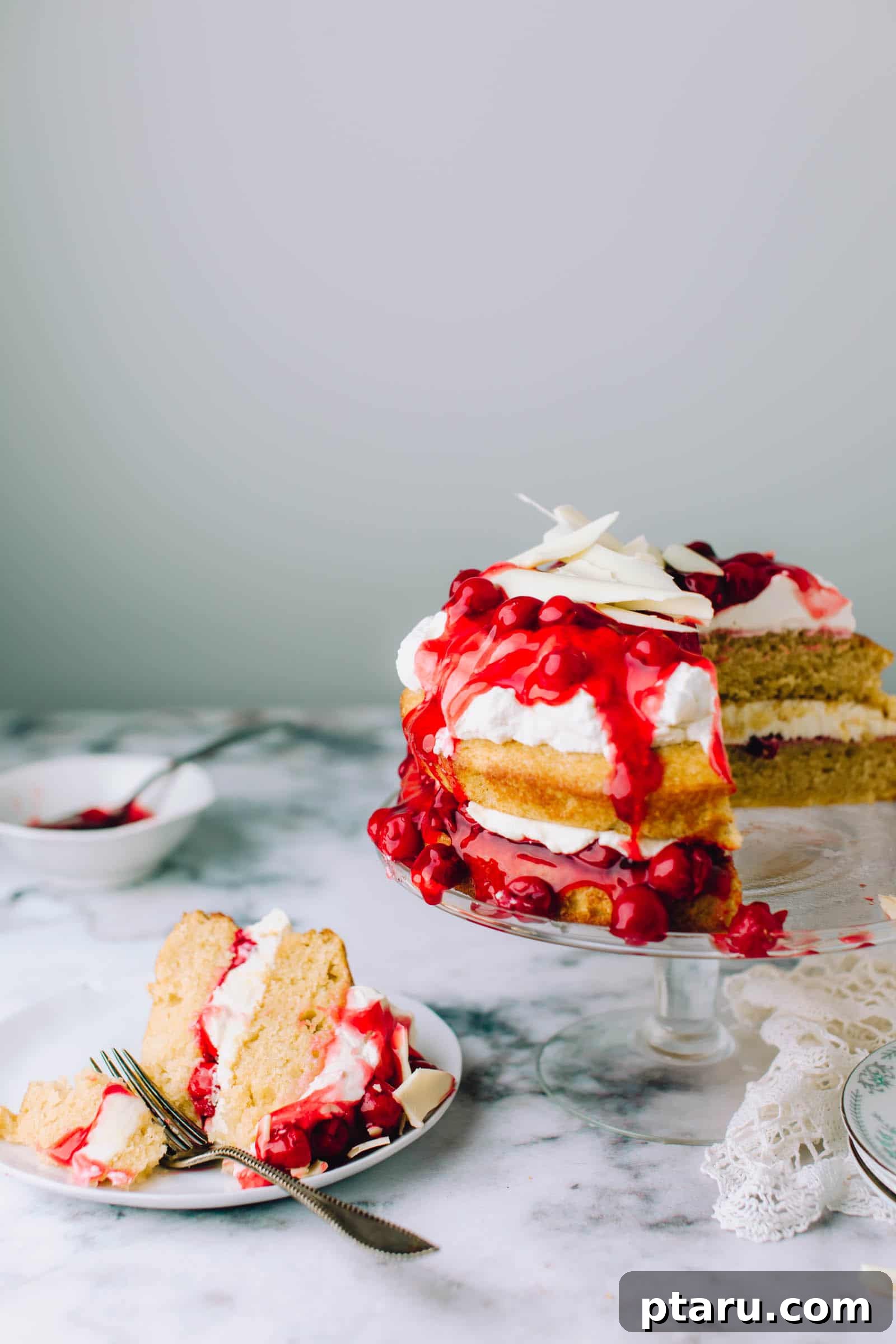 Snowy Cherry Gateau 4 Side view of a slice of White Forest Cake showcasing perfect layers of vanilla cake, white chocolate mousse, and vibrant cherry filling