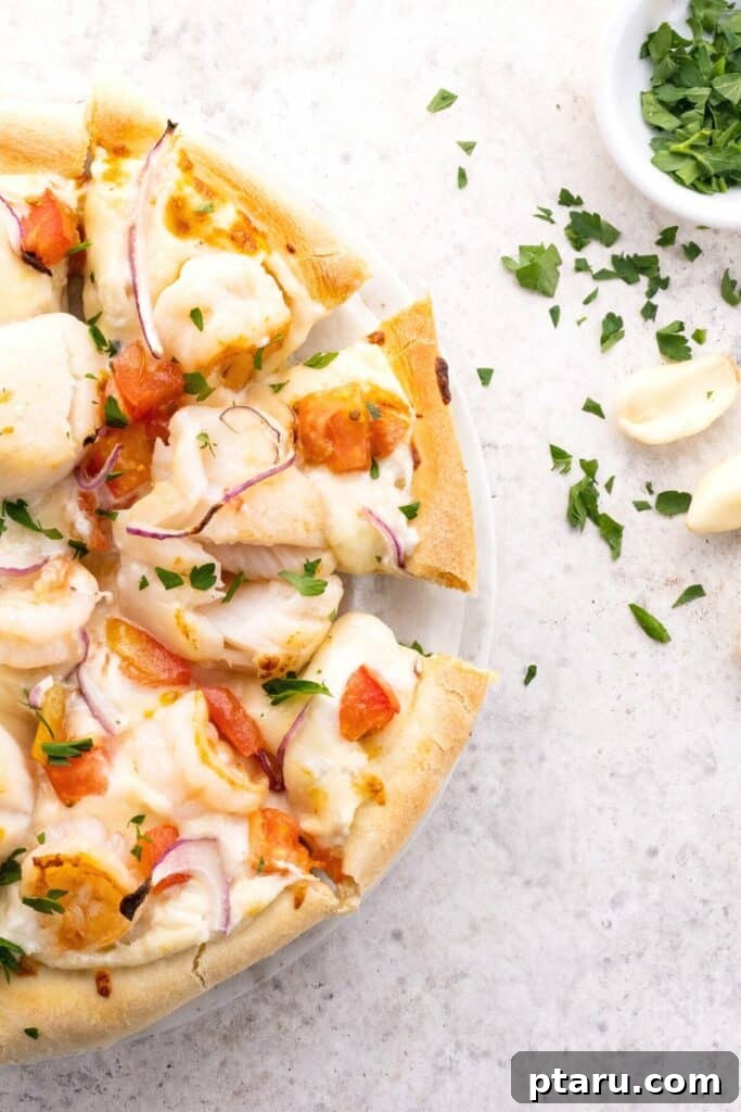 Ocean Harvest Pizza 6 Half view of delicious seafood pizza on a kitchen countertop, topped with shrimp, scallops, white sauce and a sprinkle of parsley