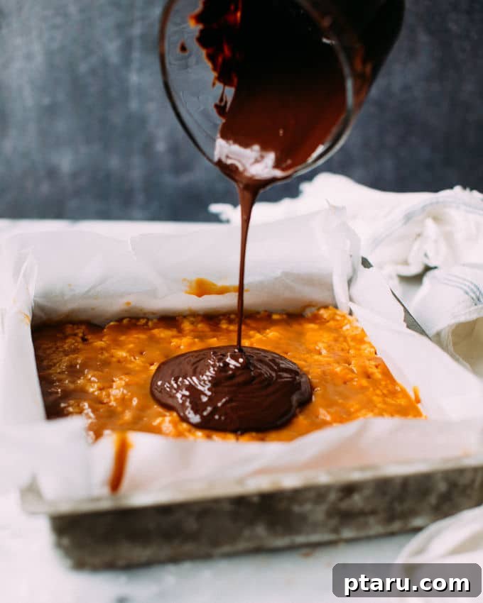 Caramel Sea Salt Krispie Bars 3 Melted dark chocolate being carefully poured from a bowl onto the firm, golden layer of salted caramel, which rests atop the peanut butter Rice Krispie treat base in a parchment-lined baking dish.