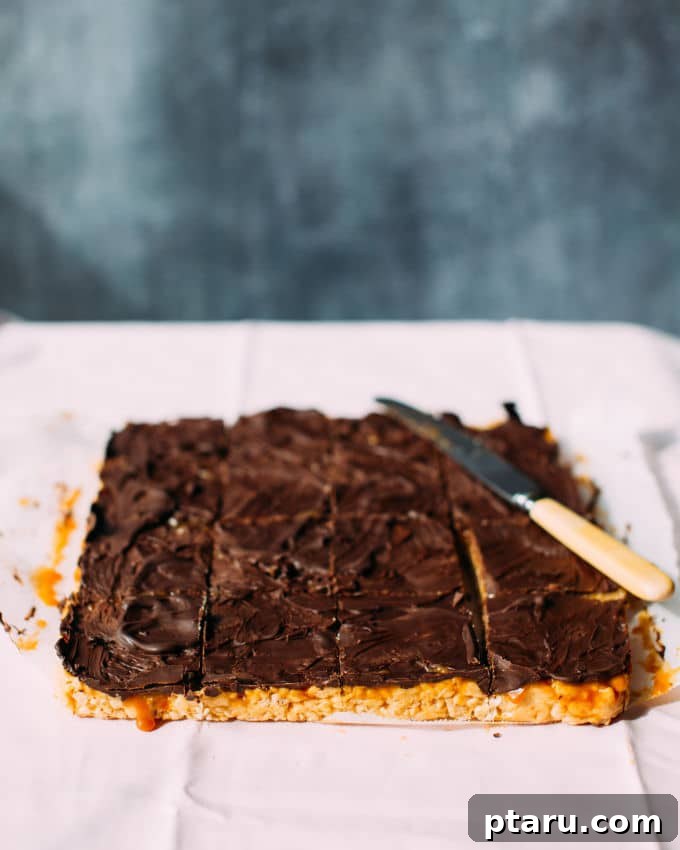 Caramel Sea Salt Krispie Bars 4 A tray of freshly set Salted Caramel Rice Krispie Treats, carefully sliced into squares, with a chef's knife resting beside them, highlighting the inviting layers of the dessert.