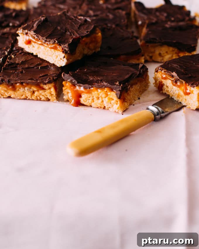 Caramel Sea Salt Krispie Bars 5 A close-up view of neatly sliced Salted Caramel Rice Krispie Treats, displaying their intricate layers of crunchy cereal, rich peanut butter, golden salted caramel, and dark chocolate. A sharp knife rests nearby.