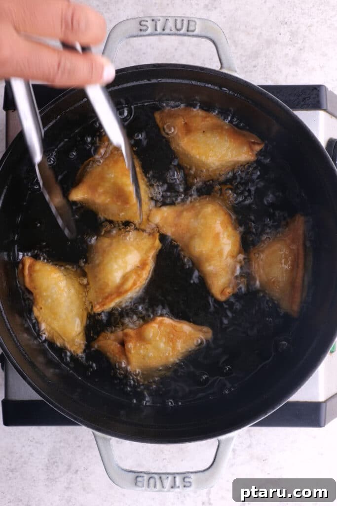 Crispy Chicken Samosas 8 Chicken Samosas being deep-fried to a golden brown in a pot.