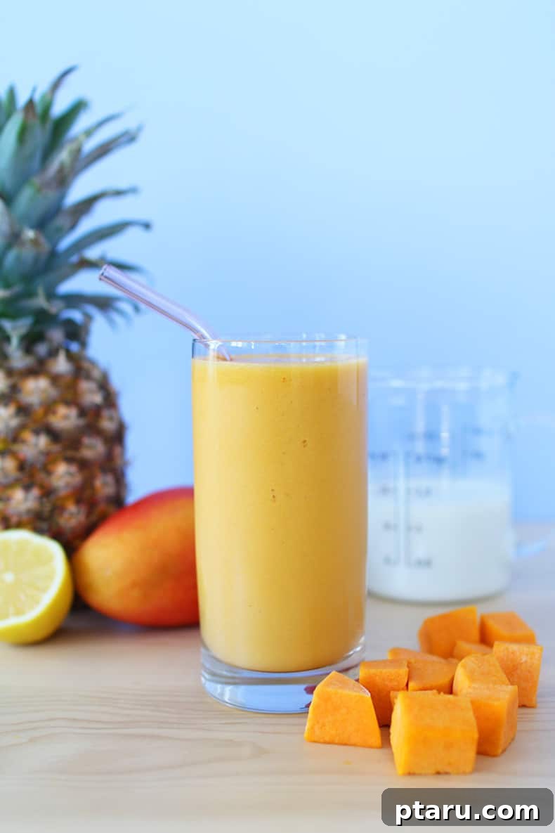 Fresh pineapple, mango, and butternut squash arranged beside a smoothie glass, indicating the healthy ingredients for a tropical glow smoothie.