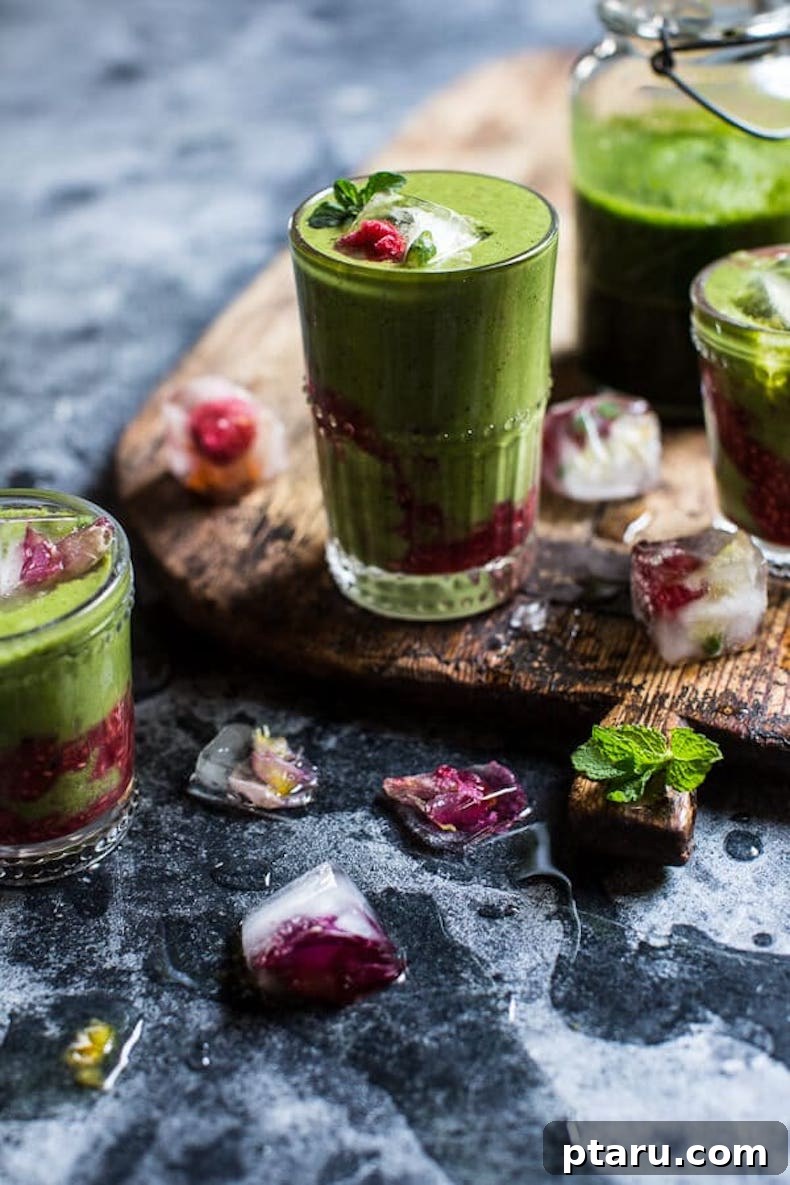 A beautifully layered green smoothie in a glass, featuring a vibrant pink raspberry swirl, suggesting a delightful blend of berries and greens with tropical notes.