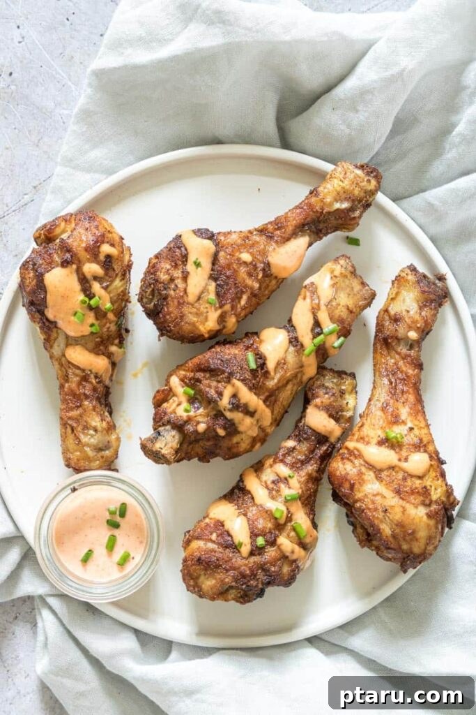 41 Succulent Chicken Drumstick Recipes You Can Make Effortlessly 14 Crispy Air Fryer Chicken Drumsticks on a white plate with a side of dipping sauce.