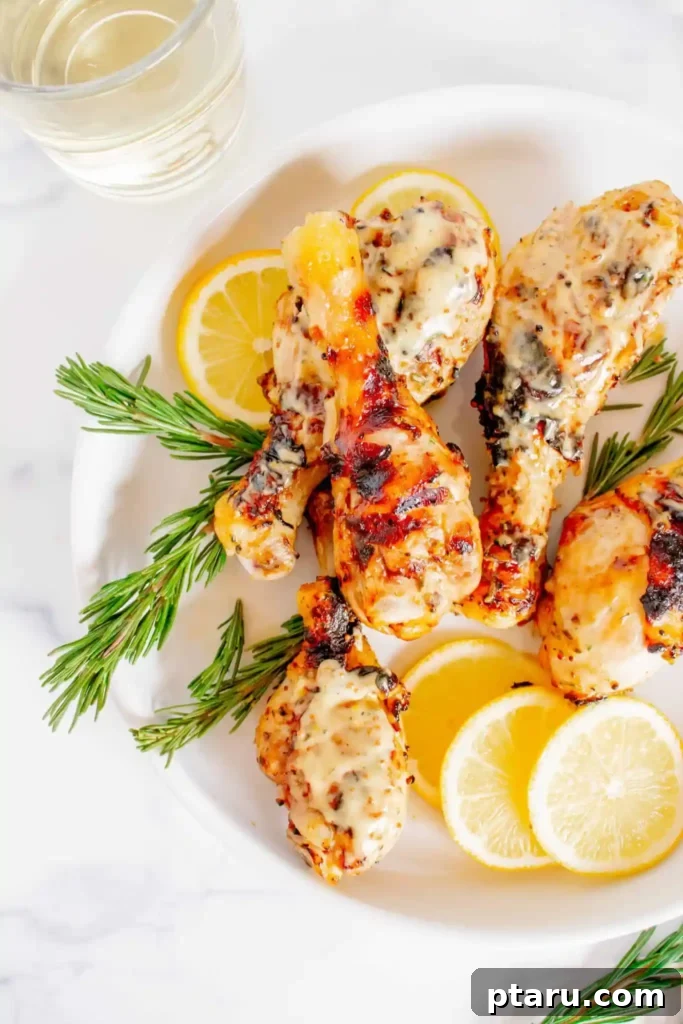 41 Succulent Chicken Drumstick Recipes You Can Make Effortlessly 16 Grilled Honey Mustard Chicken Drumsticks on a white plate with lemon slices and rosemary.
