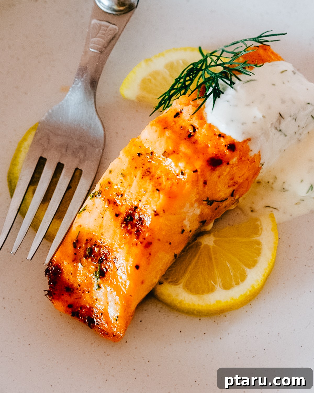 Succulent Grilled Salmon 7 Dill sauce spooned over a filet of grilled salmon on a plate with lemon slices.