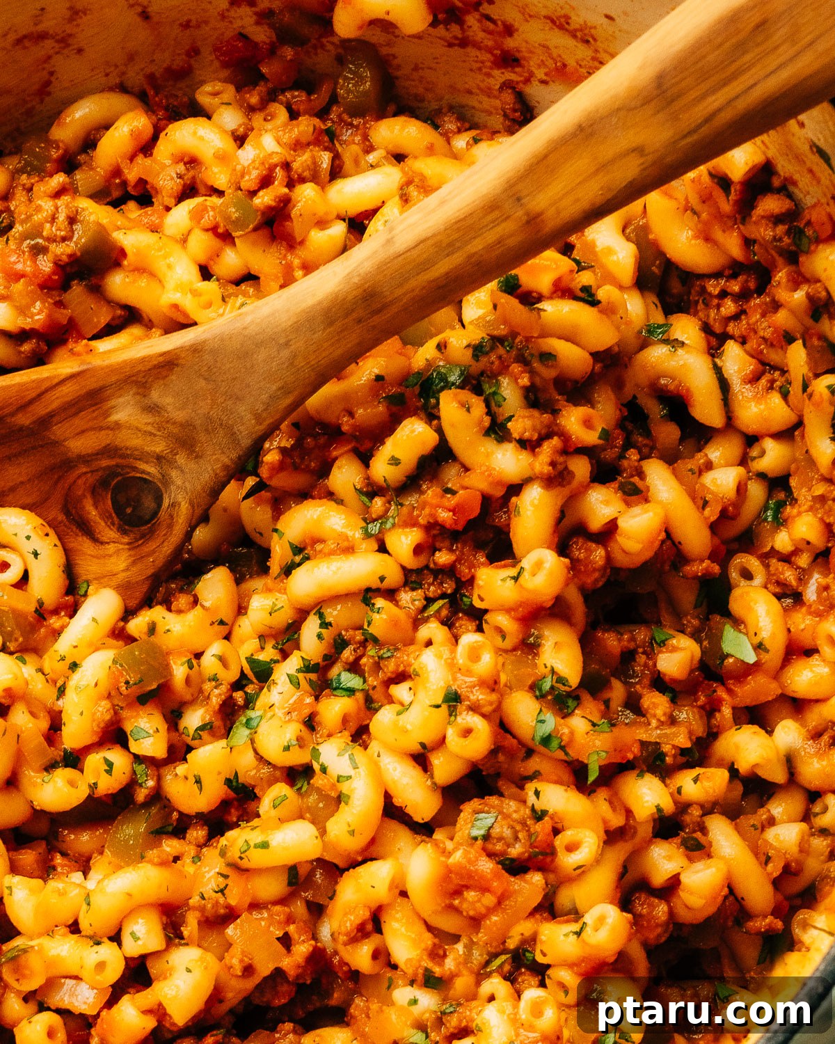 Classic Macaroni Goulash 8 A close-up view of a serving of American Chop Suey in a bowl, showing the rich sauce, ground beef, and elbow macaroni noodles, garnished with fresh parsley.