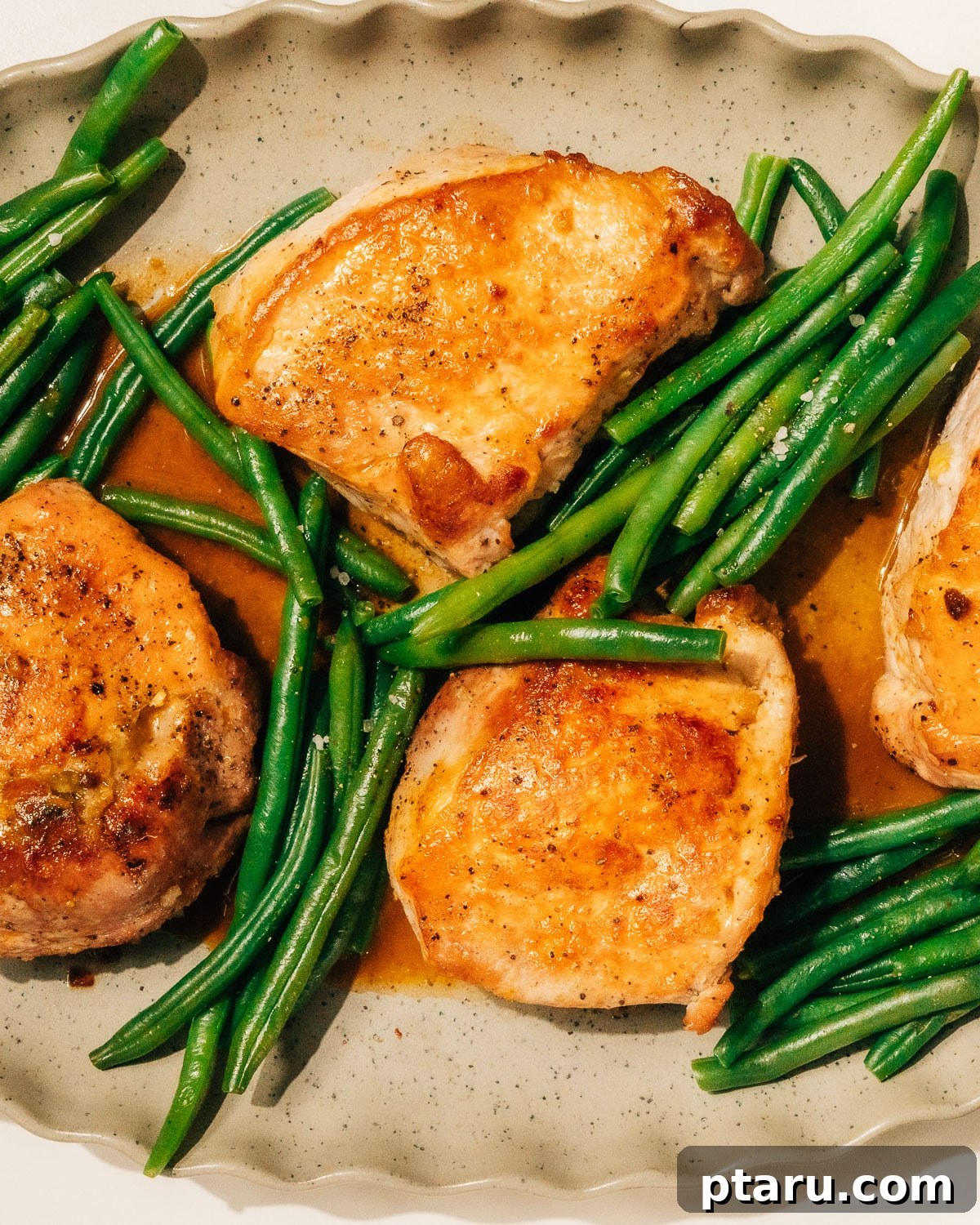 Juicy Stuffed Pork Chops with Luscious Pan Sauce 11 Two beautifully plated stuffed pork chops, accompanied by crisp green beans, drizzled with the savory pan sauce, and garnished with fresh herbs on a large serving platter.