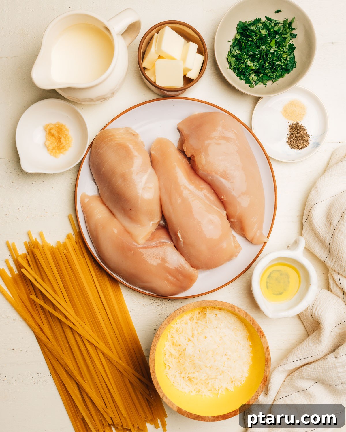 Creamy Chicken Alfredo Perfection 3 All the fresh ingredients for Chicken Alfredo, including chicken breasts, heavy cream, butter, garlic, parmesan cheese, and fettuccine, neatly arranged on a counter.