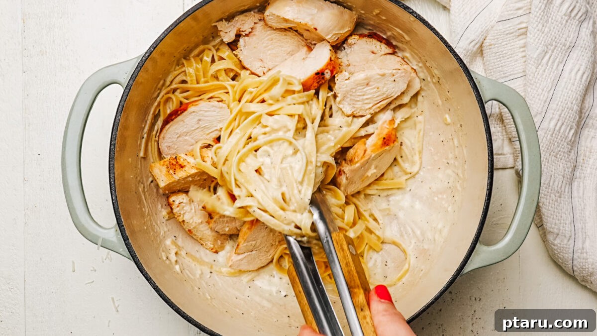 Creamy Chicken Alfredo Perfection 7 Tossing fettuccine in creamy Alfredo Sauce with sliced chicken and fresh herbs, preparing to serve.