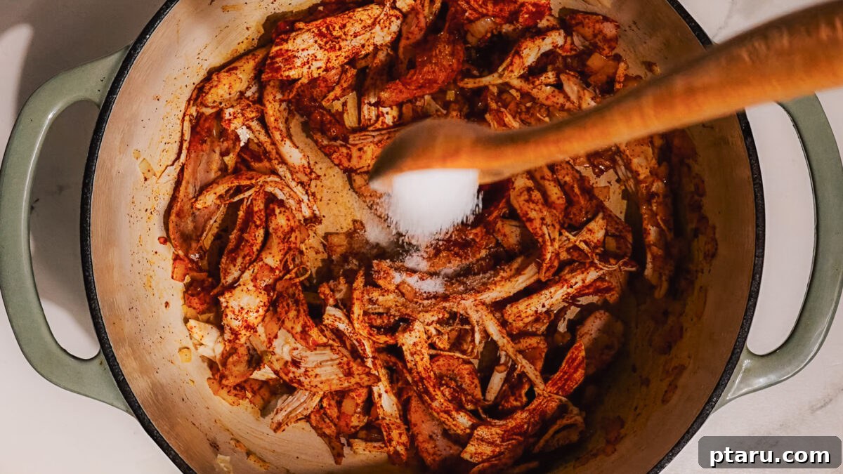 Fiesta Chicken Bake 5 Step 2: Adding shredded chicken and chili powder to the pan to season.