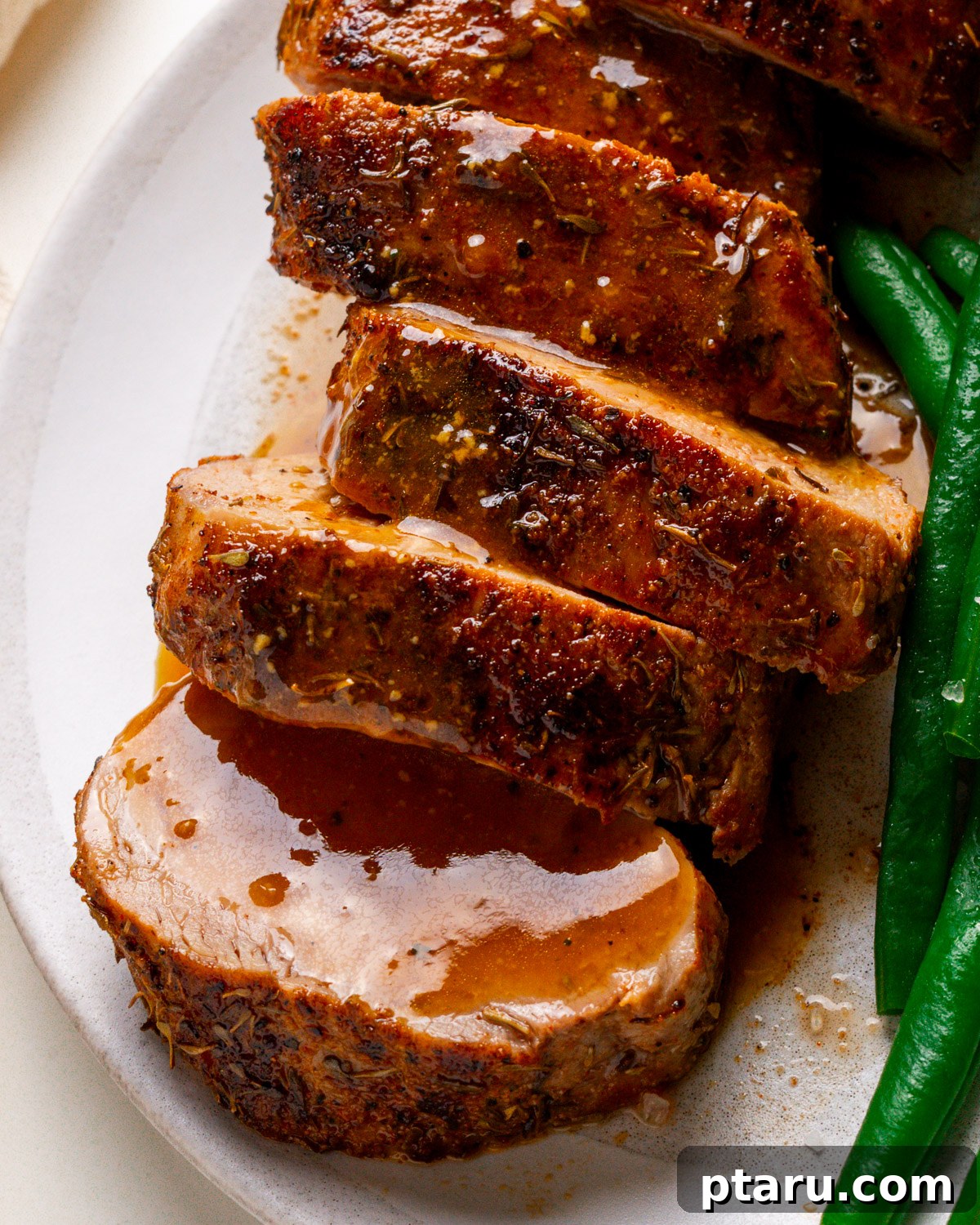 Melt-in-Your-Mouth Pork Tenderloin Recipe 2 Finished pork tenderloin recipe on a plate with sauce drizzled over.