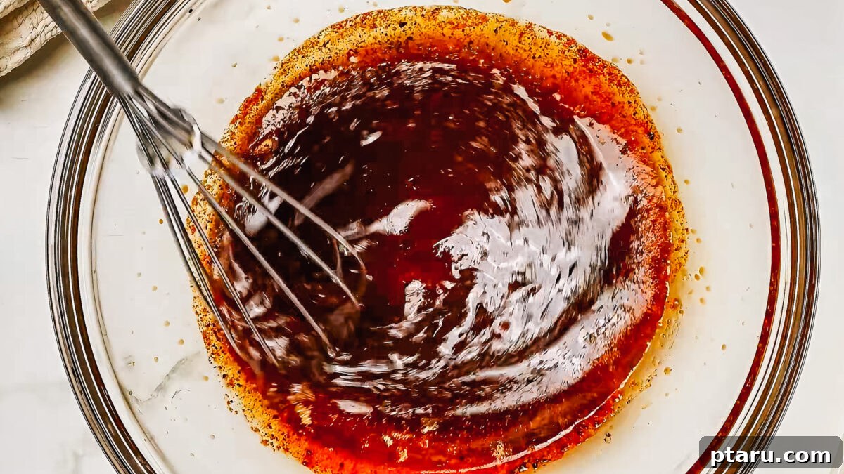 Melt-in-Your-Mouth Pork Tenderloin Marinade 4 A close-up shot of a whisk combining the liquid ingredients for the pork tenderloin marinade in a medium bowl, showing the beginning of the preparation process.