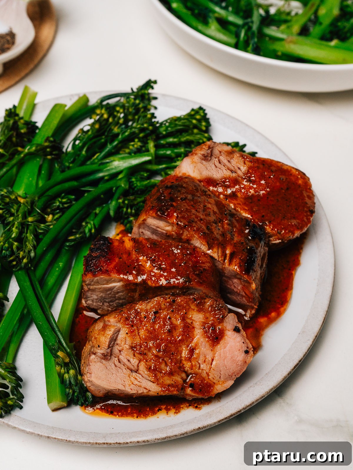 Melt-in-Your-Mouth Pork Tenderloin Marinade 7 Beautifully plated pork tenderloin medallions with a rich glaze, accompanied by vibrant green broccolini, creating an appetizing meal.