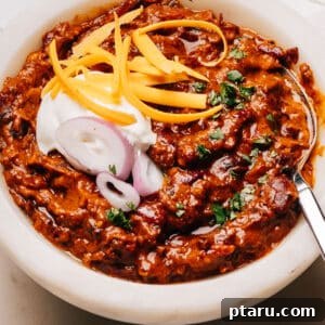 Finisheda Turkey Chili Crockpot Recipe in a bowl with a spoon, sour cream, onions and cheese.