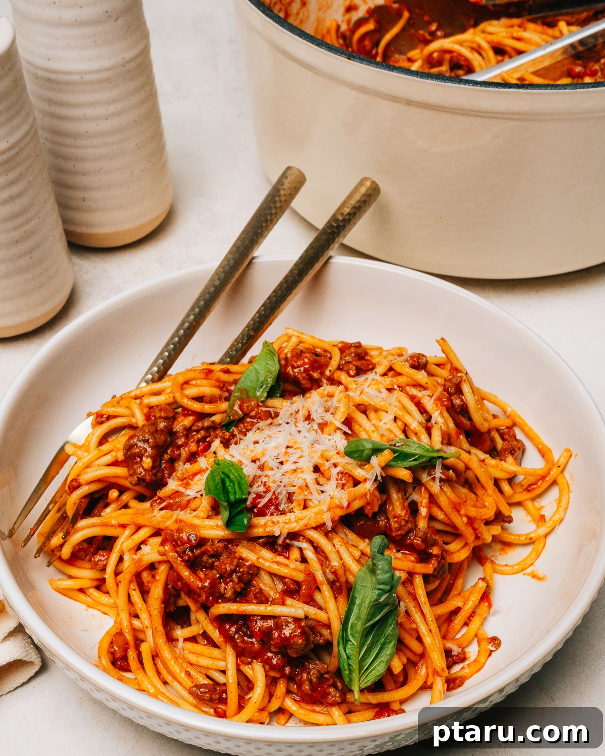 Hearty Beef Spaghetti Made Simple 8 Spaghetti with ground beef served in a white bowl, generously topped with freshly grated Parmesan cheese and a sprig of basil.