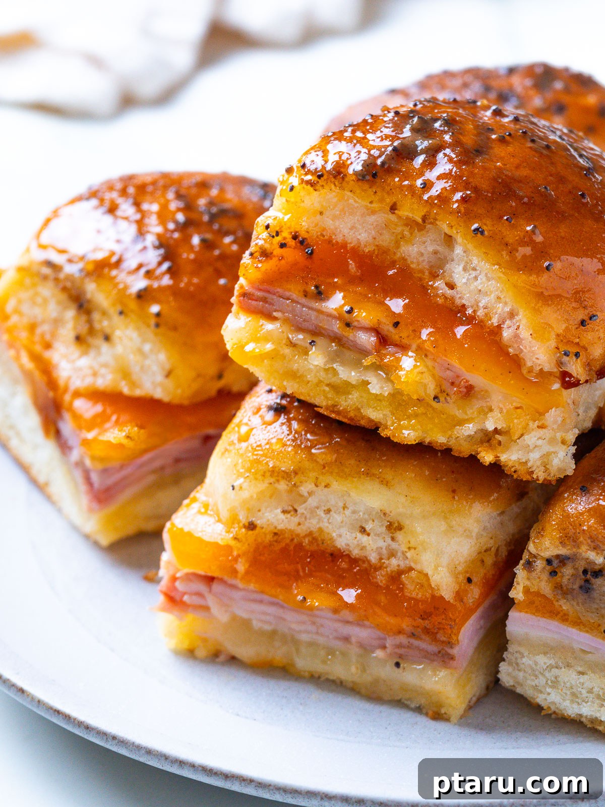 Buttery Honey-Glazed Ham & Cheese Sliders Recipe 8 A plate of stacked Hawaiian ham and cheese sliders with a glossy, poppy-seed-flecked glaze.