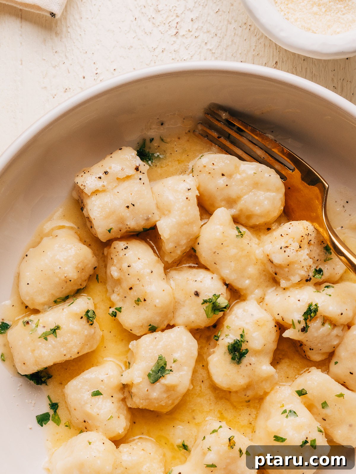 Close up of potato gnocchi tossed in butter sauce with fresh parsley and black pepper.