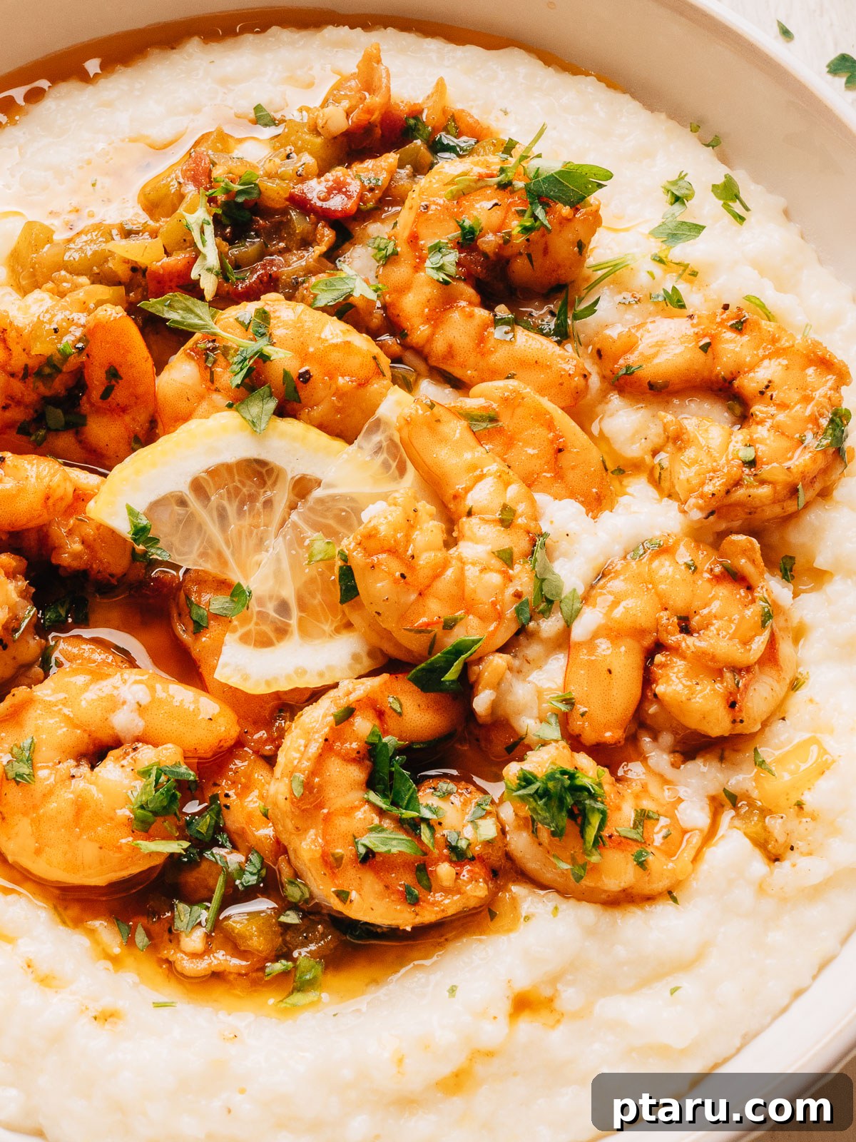 Close-up of shrimp in a smoky bacon sauce over white cheddar grits with fresh parsley.