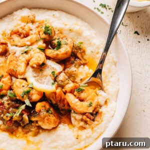 A bowl of shrimp and grits with seasoned shrimp, a bacon pan sauce, and a lemon slice over creamy cheesy grits.