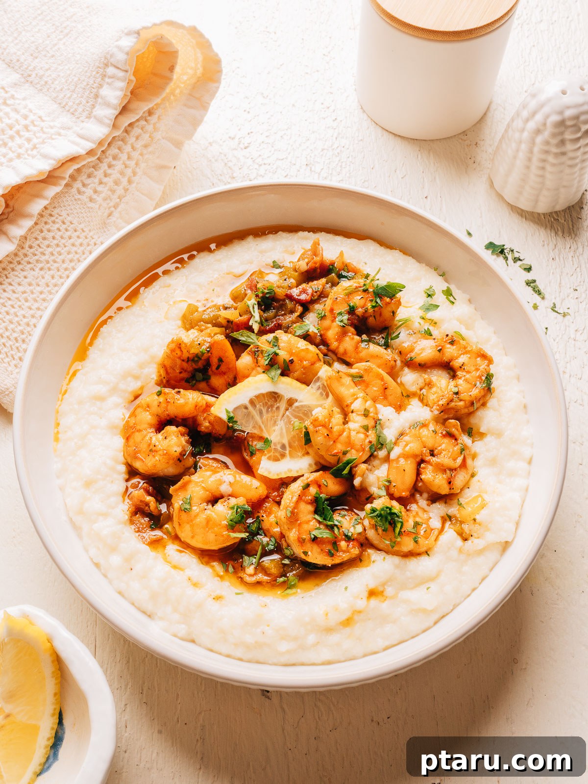 Overhead view of a white bowl of Southern shrimp and grits with parsley and a linen napkin.