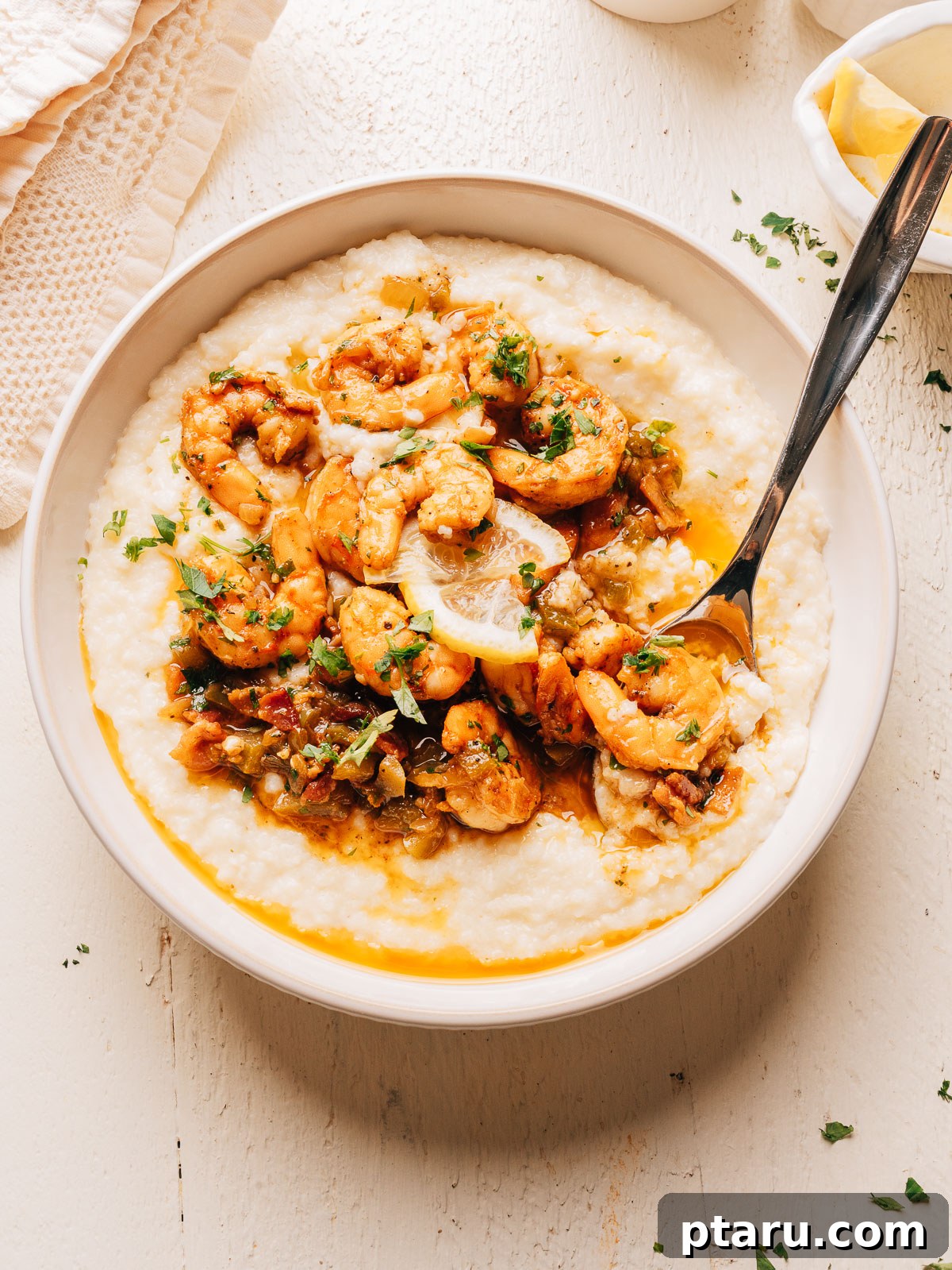 A bowl of creamy shrimp and grits with a spoon and a small dish of lemon wedges.