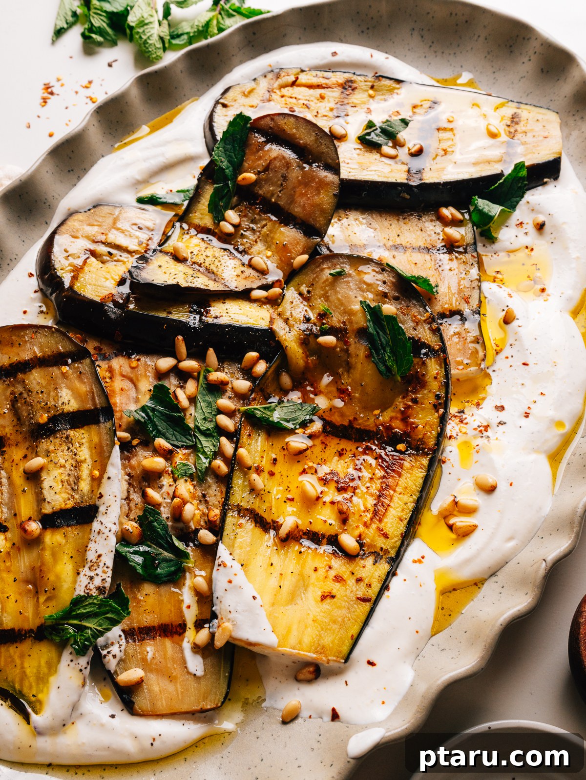 Grilled Eggplant with Garlic Oil and Whipped Feta 10 Grilled eggplant slices arranged over whipped feta with mint and pine nuts on a platter.