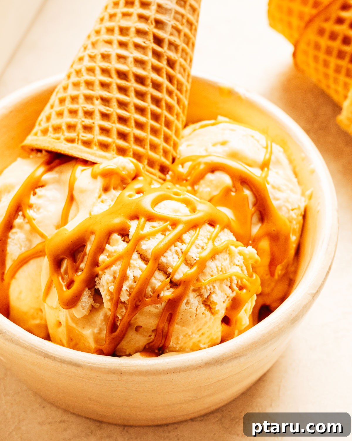 Scoops of homemade peanut butter ice cream in a bowl with peanut butter drizzled on top.