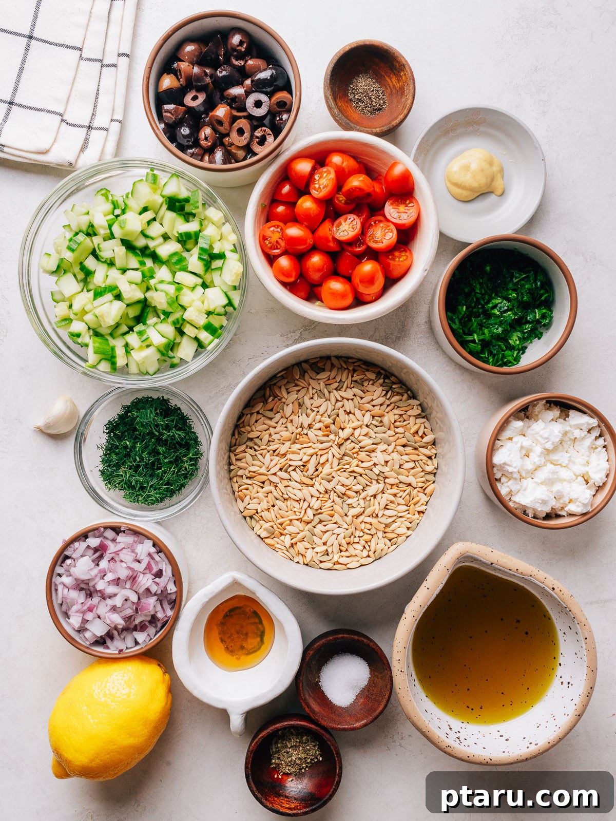 Orzo pasta salad ingredients with cucumber, cherry tomatoes, olives and feta in a bowl.