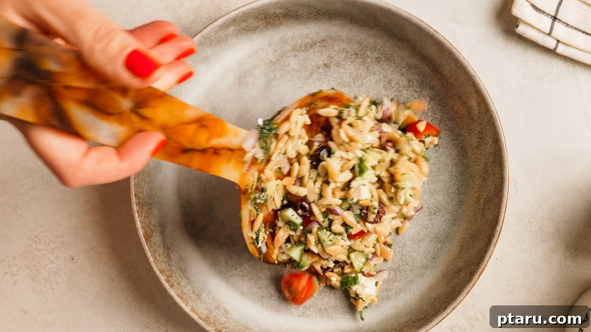 A wooden spoon lifting a serving of orzo pasta salad from the bowl.