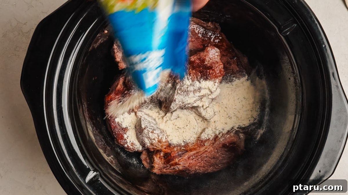 Slow-Cooker Mississippi Pot Roast 5 Ranch and au jus seasoning packets sprinkled over the roast in the slow cooker.