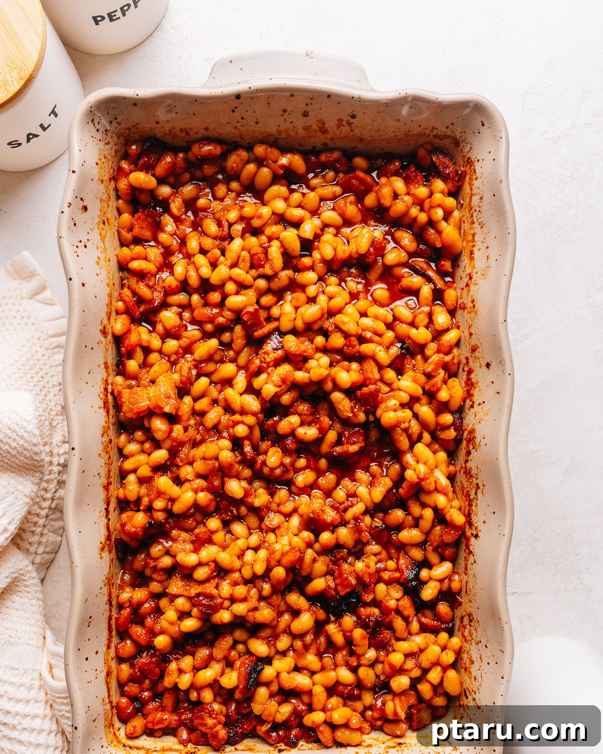 Thick Southern Baked Beans with Bacon (No-Soak Recipe) 9 Overhead view of a baking dish of baked beans beside salt and pepper cellars.