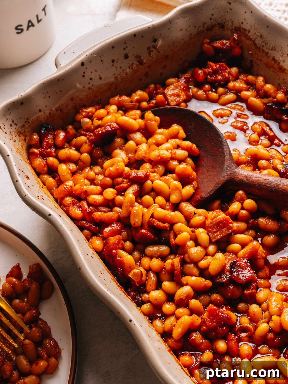 Thick Southern Baked Beans with Bacon (No-Soak Recipe) 10 Baked beans in a baking dish with a wooden spoon and a plated serving alongside.