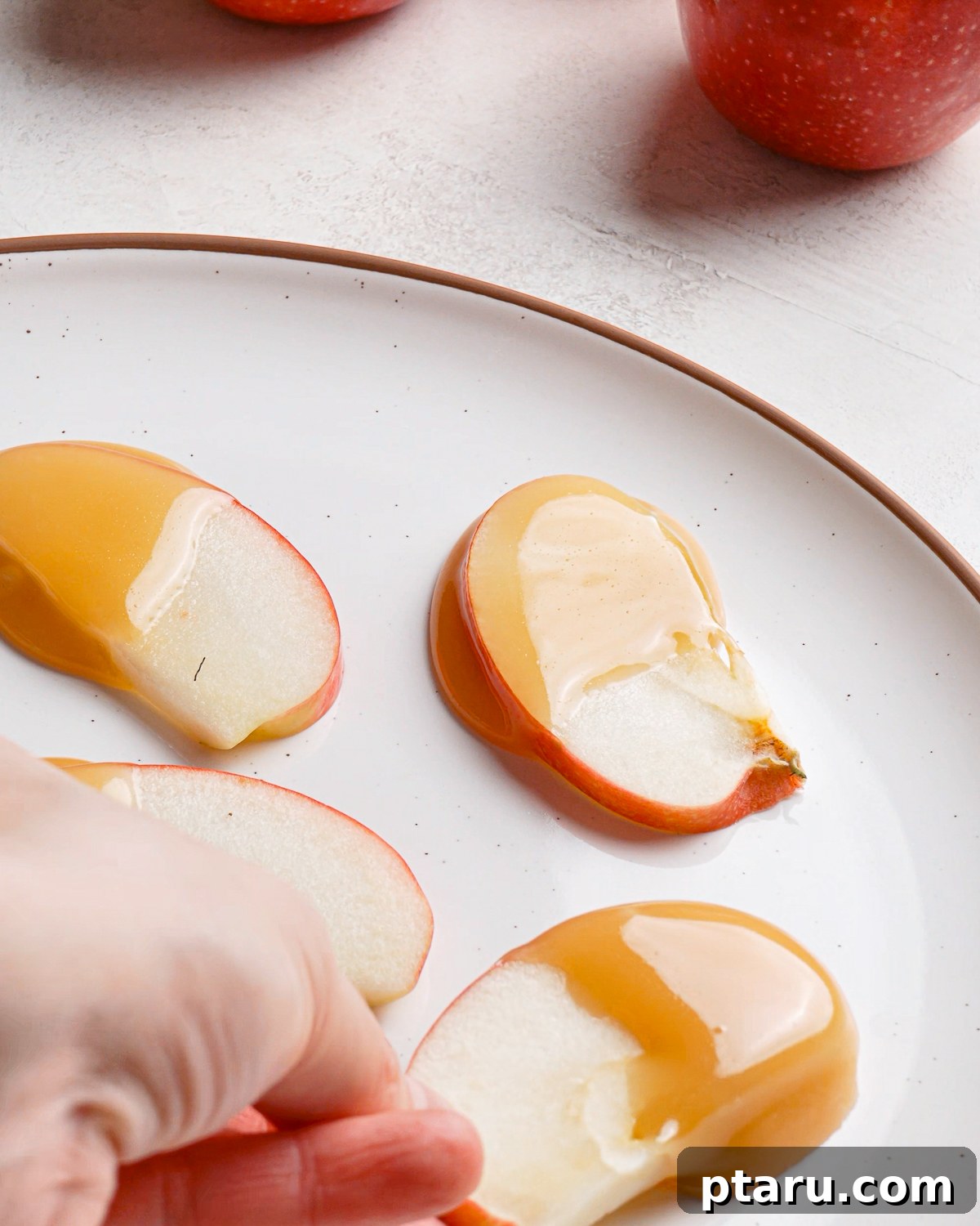 Caramel Apple Slices with Homemade Caramel Sauce 12 Picking up a caramel coated apple slice from a plate.